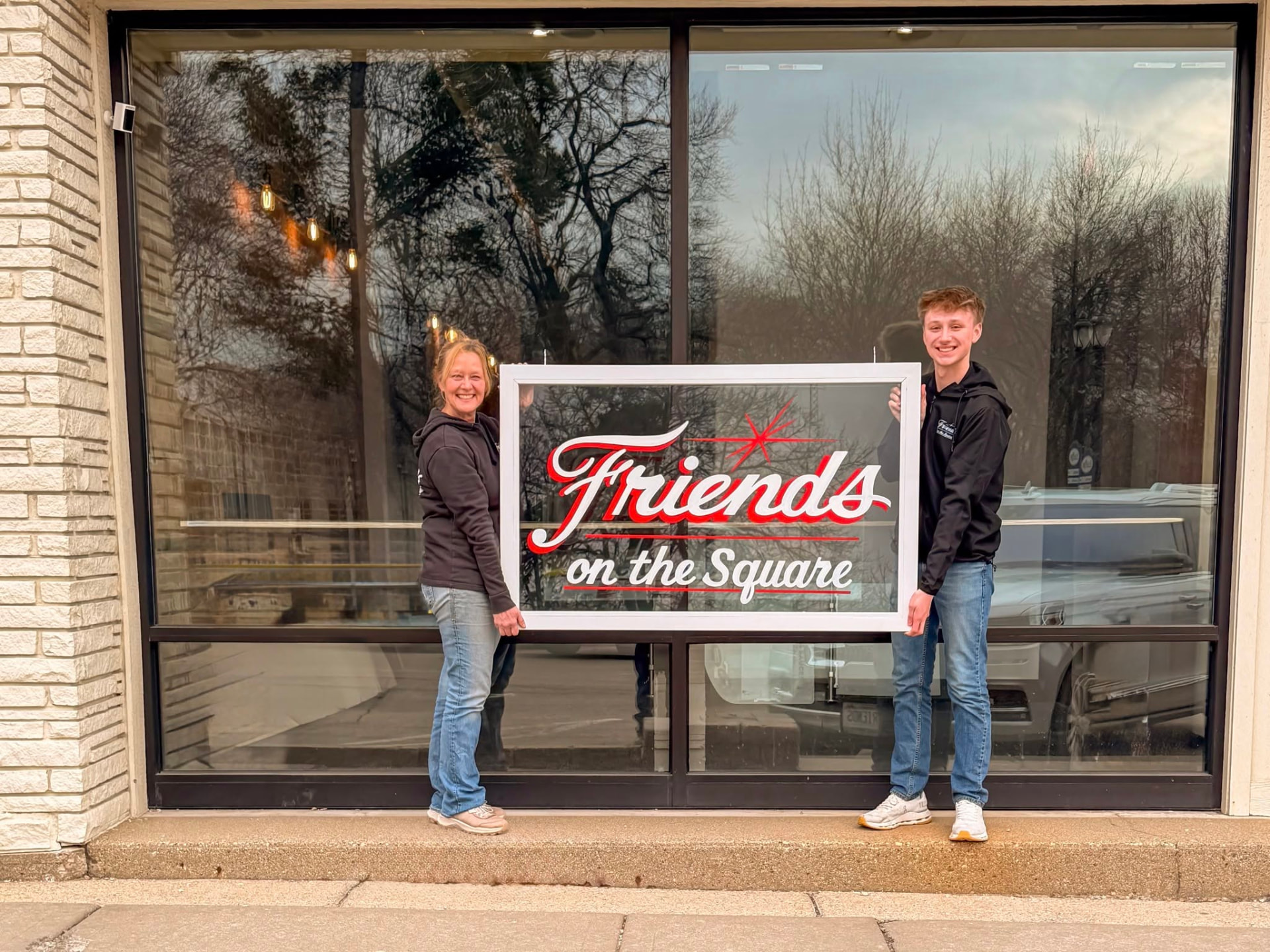 Kelly Odling, left, and David Redford, right, holding the original hand-painted Friends on the Square sign outside the shop
